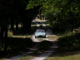 a small car driving down a dirt road in the woods