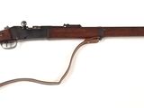 Un vieux fusil est posé sur une surface blanche, avec une sangle marron.