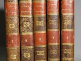 five old books are lined up in a row on a gray surface
