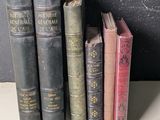 Plusieurs vieux livres sont alignés sur une étagère devant un tableau noir.