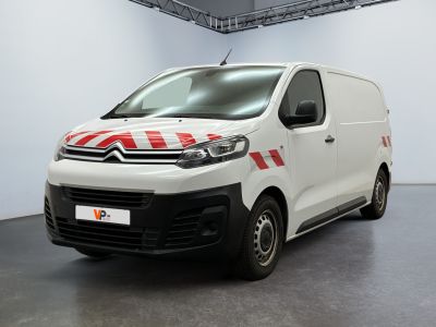 La camionnette blanche est garée dans une grande pièce ; elle porte une bande rouge et blanche sur le côté.