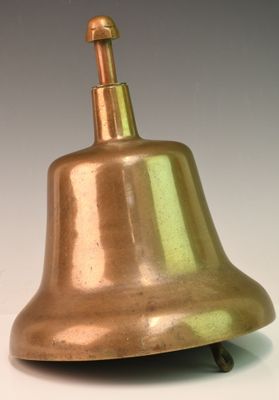 une cloche en laiton posée sur une surface blanche, avec un fond gris