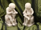 pair of white statues of a man and a woman sitting on a bench