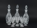 four clear glass wine glasses and a decanter on a black background