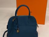 a small blue handbag next to an orange box on a white surface
