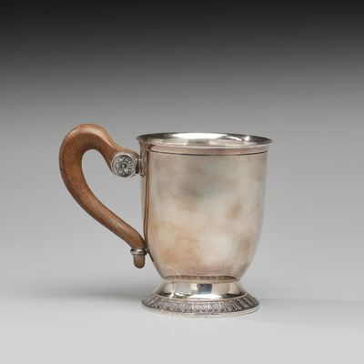 une coupe ancienne en argent, munie d'une poignée en bois, posée sur une surface blanche