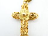 a gold cross pendant with filigree design on a white background