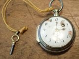 a silver pocket watch and a key on a wooden table