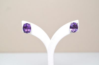 une paire de boucles d'oreilles en améthorate posée sur un socle blanc, sur une table