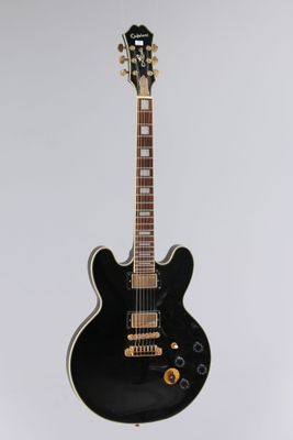 a black electric guitar sitting on top of a white surface