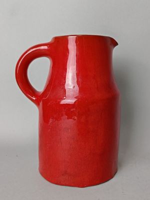 un vase rouge muni d'une anse, posé sur une table