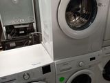 Plusieurs lave-linge et sèche-linge sont empilés sur des palettes dans un entrepôt