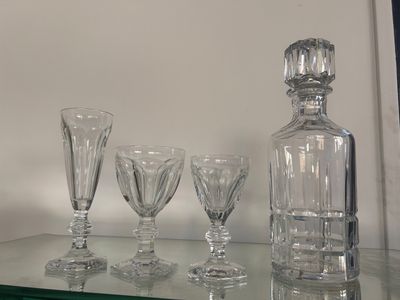 Des bouteilles et des verres sont posés sur une étagère en verre devant un mur blanc.
