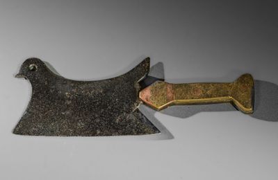 un couteau en forme d'oiseau avec un manche en métal posé sur une surface blanche