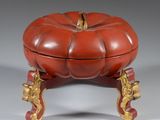 une boîte rouge et dorée en forme de citrouille posée sur un socle