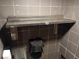 a metal shelf above a toilet in a public restroom