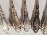 six silver spoons are lined up in a row on a white surface