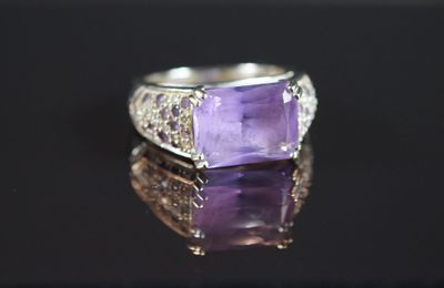 une photo d'une bague sertie d'une pierre violette, posée sur une surface réfléchissante