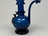 a blue glass vase with a black handle on a white table