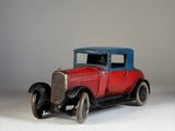 une petite voiture rouge avec un toit bleu posée sur une surface blanche
