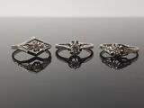 trois bagues en diamant posées sur une surface noire, avec un reflet