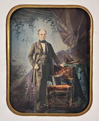 an old picture of a man in a suit standing next to a chair