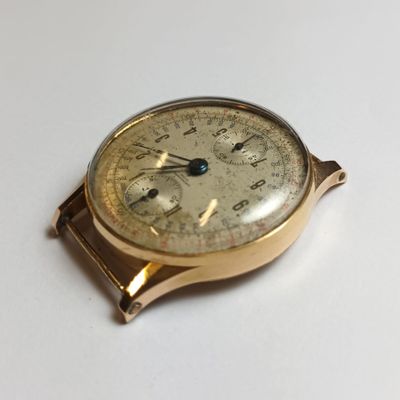 une montre en or posée sur une surface blanche, avec une trotteuse bleue