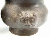 a metal vase with a face on it on a white surface