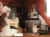 two dolls sitting on a table in a doll house