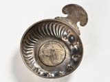 a silver spoon with a coin in it on a white surface