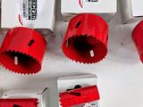 six red hole saws sitting on top of a table next to boxes of holes