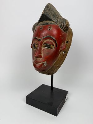 un masque en bois au visage rouge posé sur un socle noir