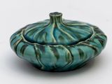 un bol bleu et vert avec un couvercle, posé sur une surface blanche