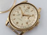 une montre en or et une loupe posées sur une surface blanche