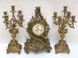 three gold colored candlesticks and a clock on a table