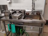 une cuisine avec un évier en inox et un tuyau d'arrosage vert posé par terre