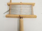 un petit métier à tisser muni d'une poignée en bois, posé sur une surface blanche
