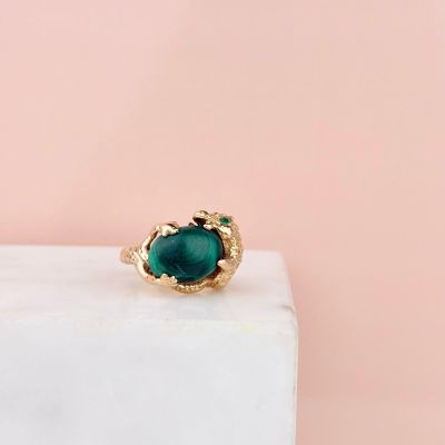 a gold ring with a green stone on top of a marble block