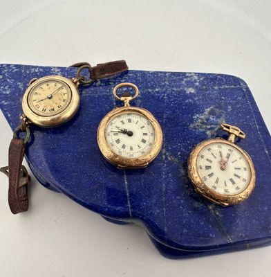 three different types of pocket watches on a blue stone slab