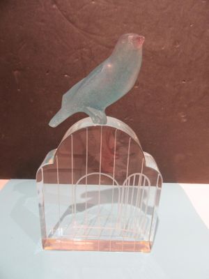 a bird sitting on top of a birdcage on a table