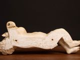 a white sculpture of a woman laying on a wooden table
