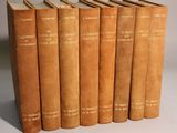 six old books are lined up in a row on a white surface
