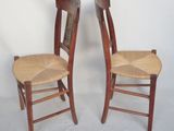 pair of wooden chairs with wicker seats against a white backdrop