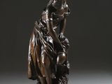 une statue antique en bronze représentant une femme assise sur un rocher