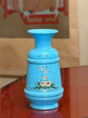 a blue vase sitting on a glass table with a picture in the background