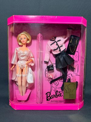 une boîte rose contenant deux poupées Barbie, sur fond noir