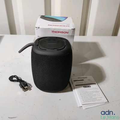 une enceinte noire posée sur une table à côté d'un chargeur