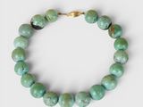 a close up of a bracelet with green beads on a white background