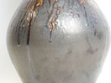 a gray vase with a brown handle sitting on a white surface