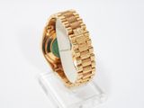 an image of a gold watch with a green face on a clear stand